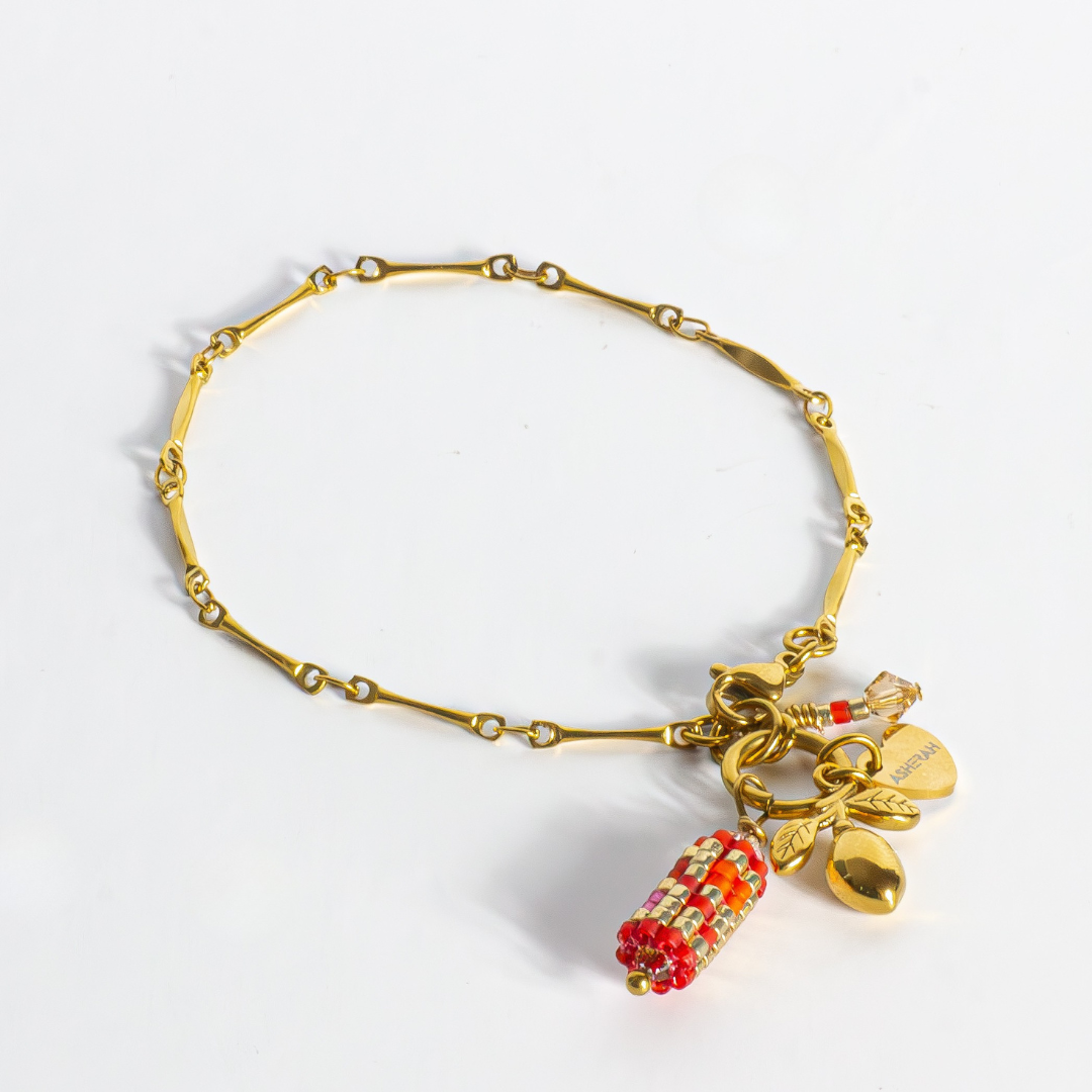 Tatreez charm bracelet in orange-red, orange, bubblegum pink, pink mist and gold on white background. Features cylindrical Tatreez charm and olive charm on fancy gold stainless steel chain.