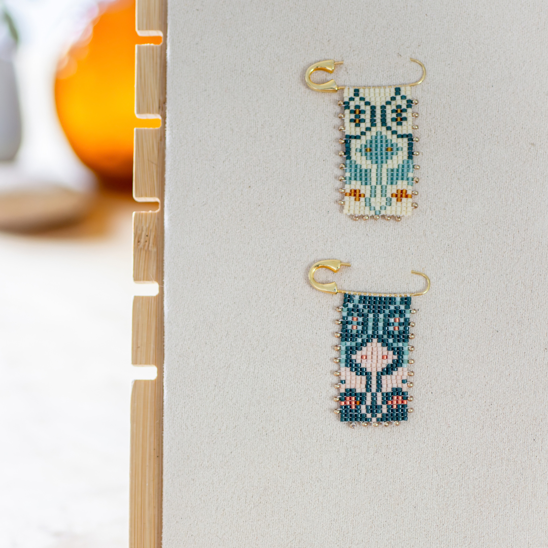 Two hand-beaded Tatreez brooches side by side — marigold and sea glass green, and evergreen and papaya orange. Tum Al Samakeh Snapdragon motif on gold-finish 925 sterling silver.