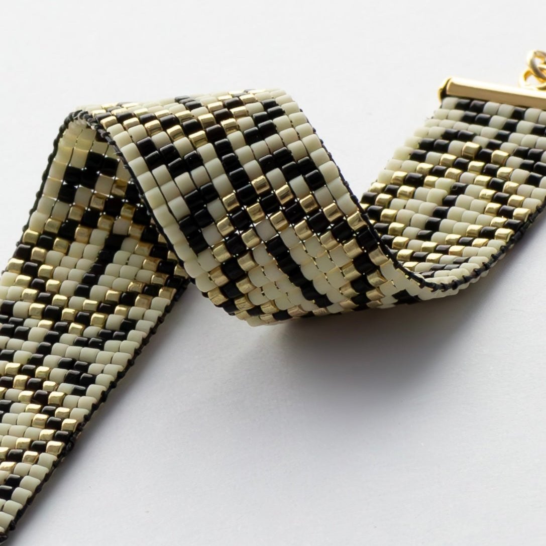 Amulet Bracelet from Al Khalil featuring the Palestinian Tatreez pattern in dark cream, black, and gold accents.