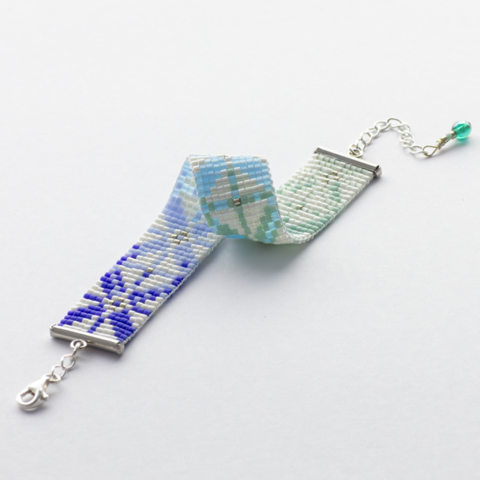 The Chain bracelet showcasing a Tatreez pattern from Yafa in green, blue and white.