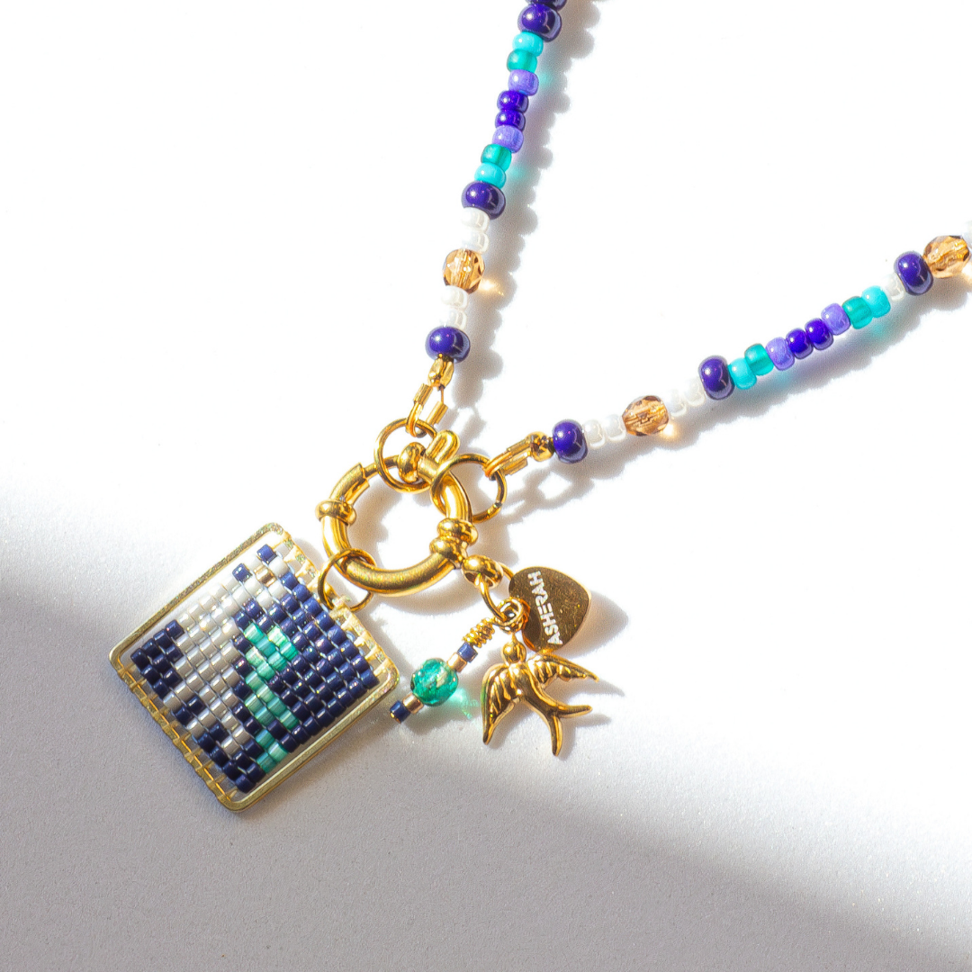 Close-up of European Roller beaded bird charm in teal, sky blue, chestnut brown, cream cylon and gold. Tatreez pattern. Agate and glass beads.