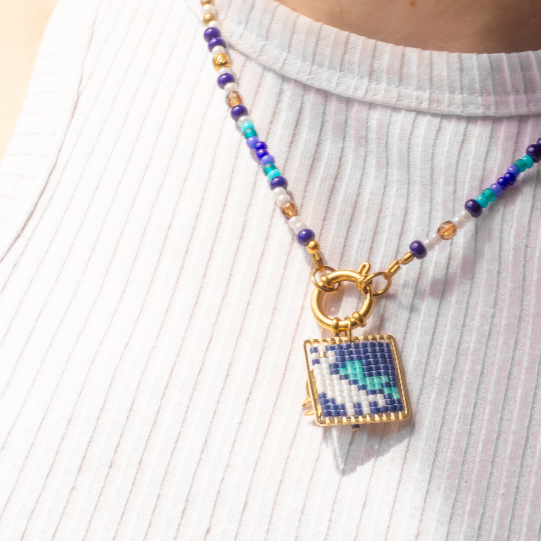 European Roller beaded necklace worn on model. Teal, sky blue, chestnut brown, cream cylon and gold beads. Agate and glass charm.