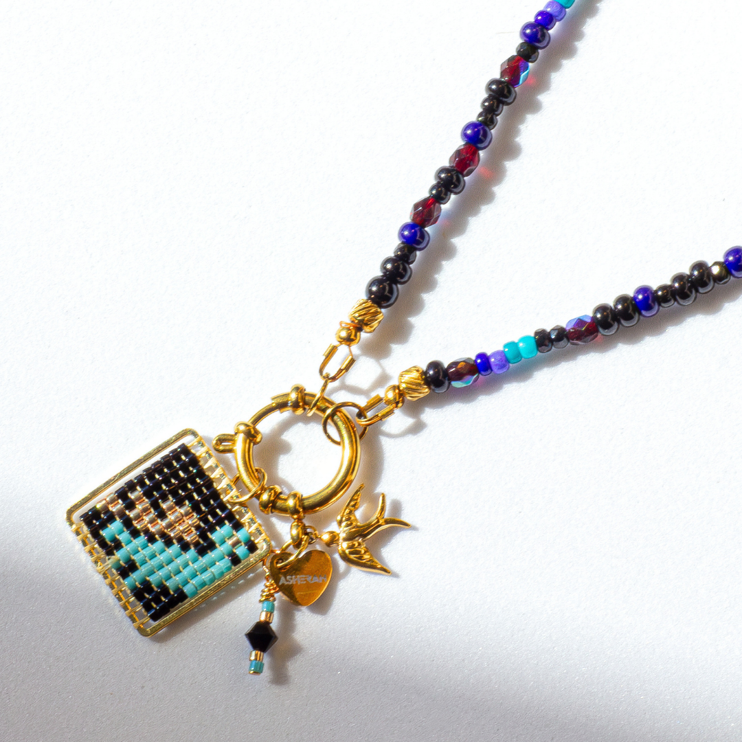 Close-up of Palestine Sunbird beaded bird charm in black with metallic blue and green highlights. Tatreez pattern. Agate and glass beads.