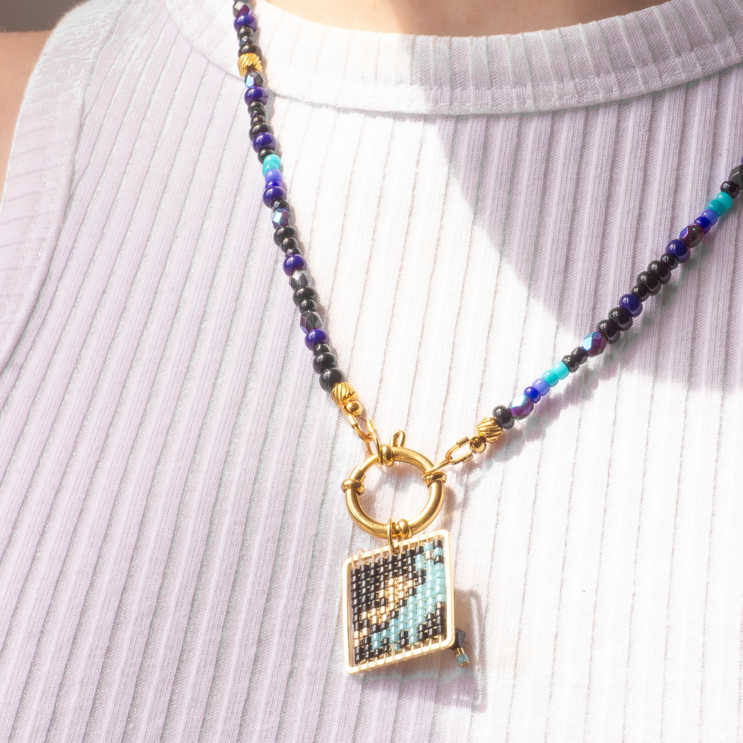 Palestine Sunbird beaded necklace worn on model. Black beads with metallic blue and green highlights. Agate and glass charm.