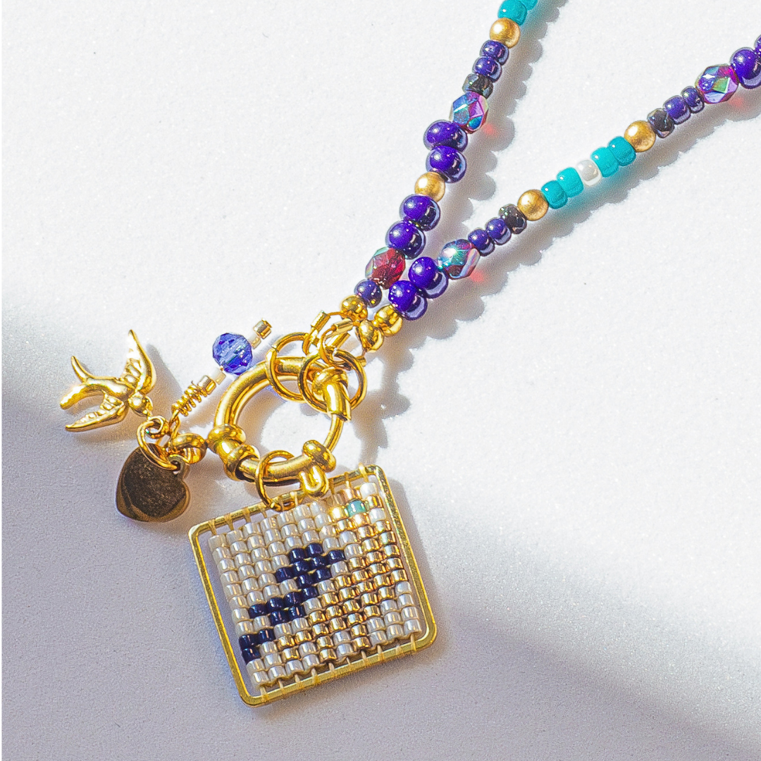 Close-up of Palestine Sunbird beaded bird charm in navy blue with metallic green and blue highlights. Tatreez pattern. Agate and glass beads.