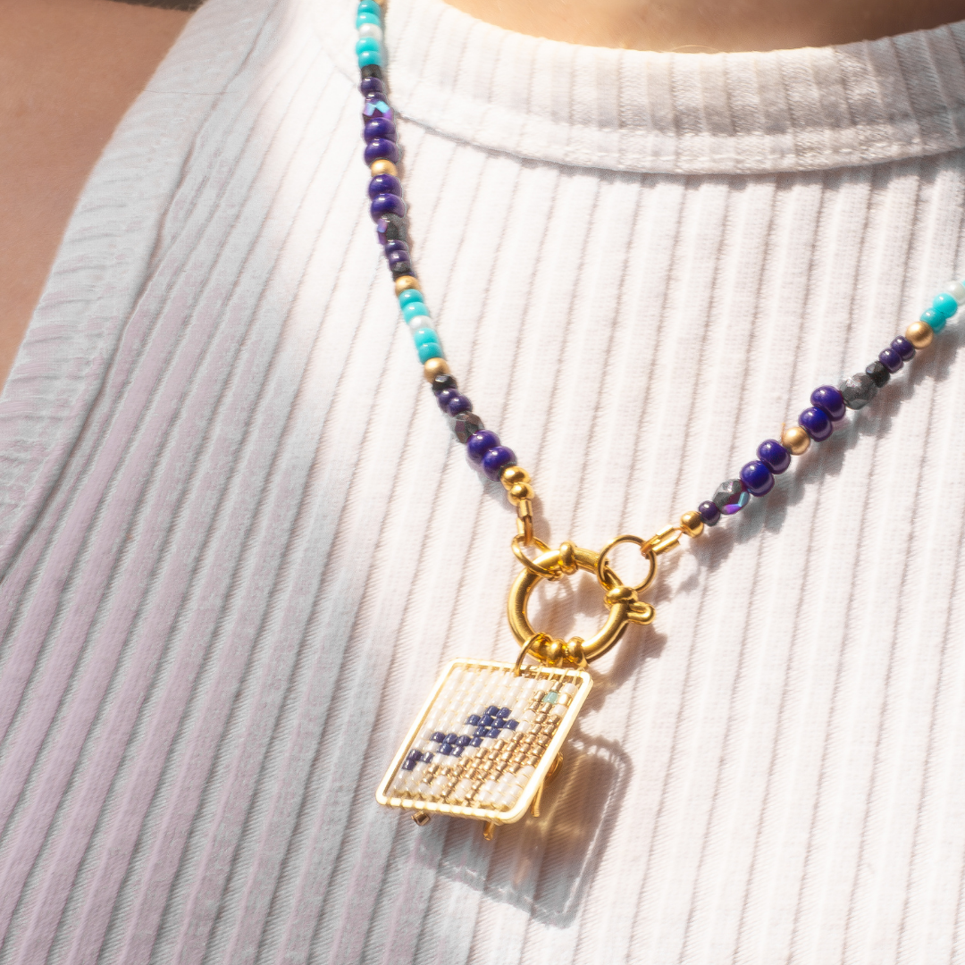 Palestine Sunbird beaded necklace worn on model. Navy blue beads with metallic green and blue highlights. Agate and glass charm.