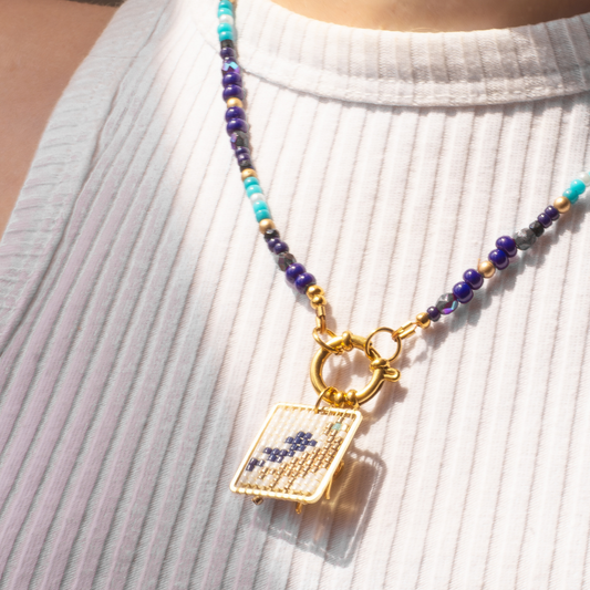 Palestine Sunbird beaded necklace worn on model. Navy blue beads with metallic green and blue highlights. Agate and glass charm.