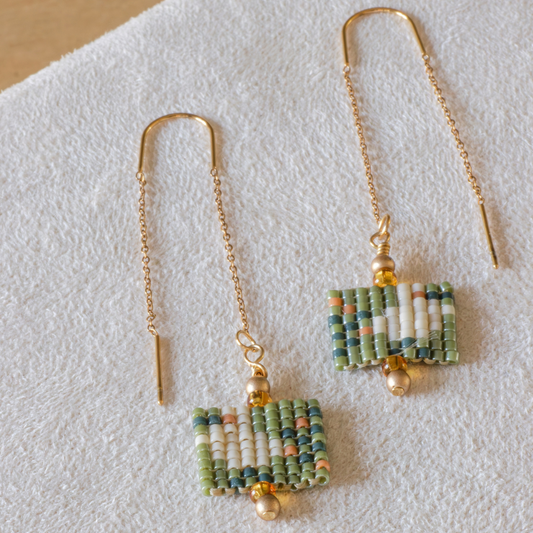 Hand-beaded Tatreez threader earrings in cactus green, cedar brown, evergreen and dark cream on white background. Asafir bird motif in Miyuki Delica beads on 304L stainless steel.