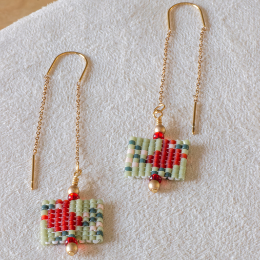 Hand-beaded Tatreez threader earrings in fennel green, evergreen, orange red and light salmon on white background. Asafir bird motif in Miyuki Delica beads on 304L stainless steel.