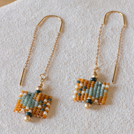 Hand-beaded Tatreez threader earrings in marigold, sea glass green, evergreen and dark cream on white background. Asafir bird motif in Miyuki Delica beads on 304L stainless steel.