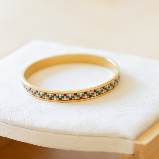 Hand-beaded Tatreez bangle in fennel green, evergreen, orange red and light salmon on white background. Three-row Miyuki glass bead pattern on 304 stainless steel.