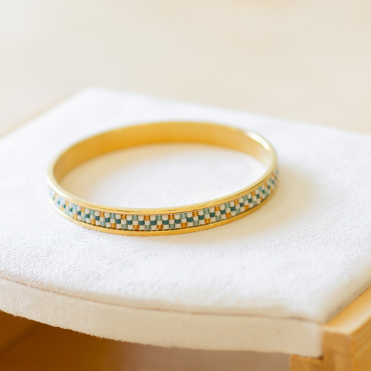 Hand-beaded Tatreez bangle in marigold, sea glass green, evergreen and dark cream on white background. Three-row Miyuki glass bead pattern on 304 stainless steel.