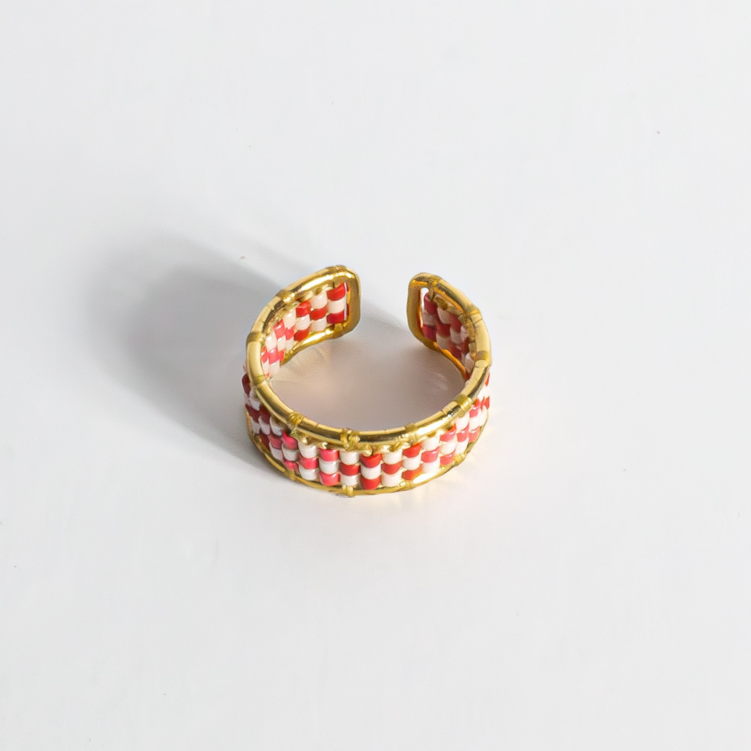 Hand-beaded Tatreez ring in brick red, pink champagne, gold and cranberry on white background. Side view showing profile. Gold filled setting.