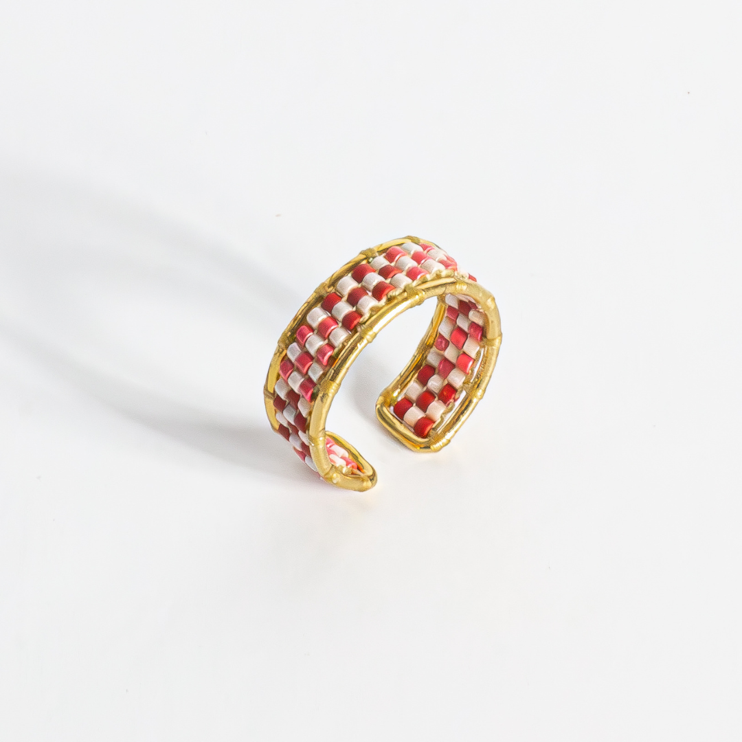 Hand-beaded Tatreez ring in brick red, pink champagne, gold and cranberry on white background. Side view showing profile. Gold filled setting.