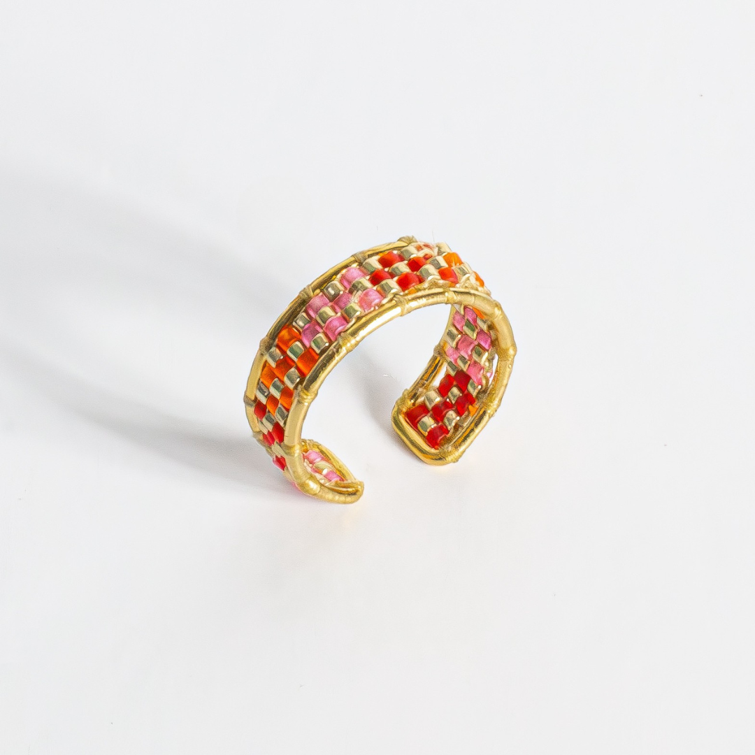 Hand-beaded Tatreez ring in orange-red, orange, bubblegum pink, pink mist and gold on white background. Front view.Gold Filled setting.
