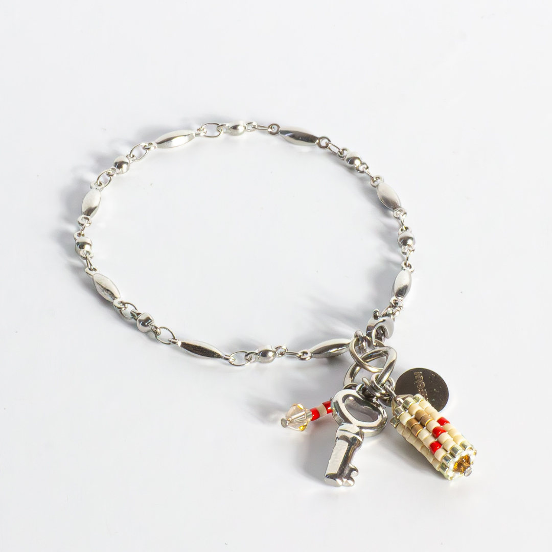 Tatreez charm bracelet in true red, silver, antique beige, sea foam and champagne on white background. Features cylindrical Tatreez charm and Key of Return charm on fancy silver stainless steel chain.