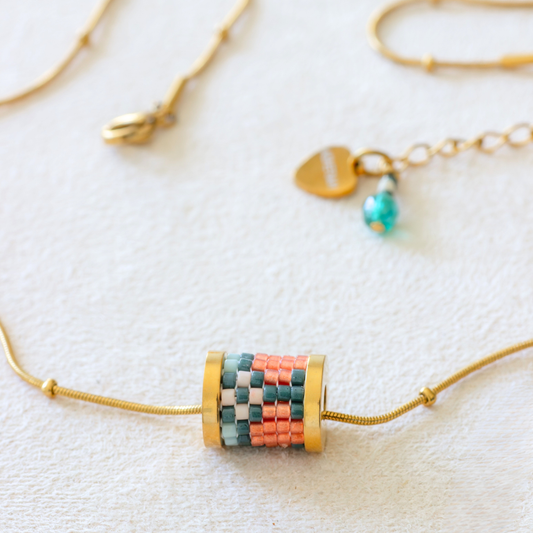 Hand-beaded Tatreez tube necklace in evergreen, pale turquoise, rose and papaya orange on white background. Miyuki glass beads on 304L stainless steel serpentine choker.