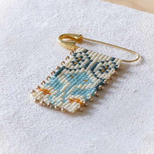 Hand-beaded Tatreez brooch in marigold, sea glass green, evergreen and dark cream. Tum Al Samakeh Snapdragon motif on gold-finish 925 sterling silver.