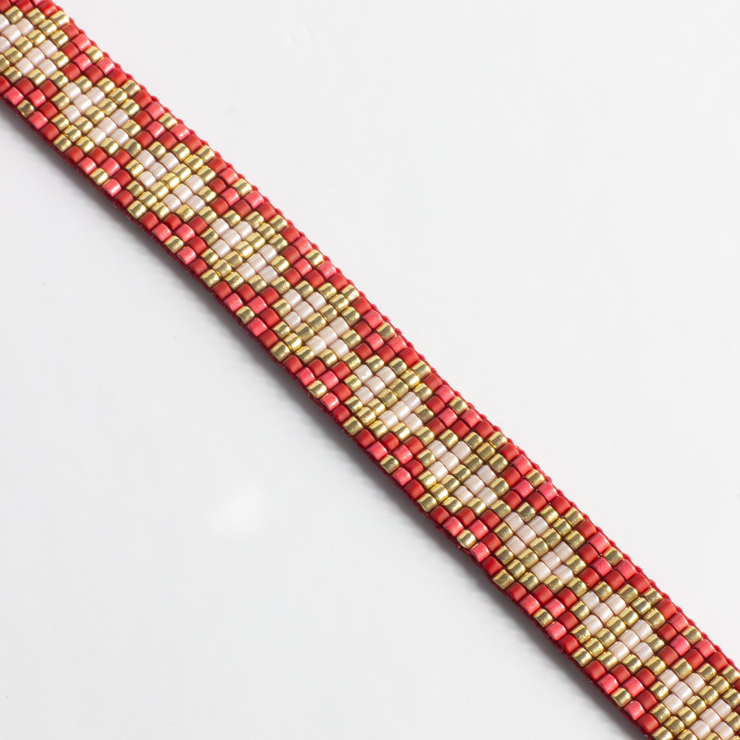 Close-up of hand-beaded Tatreez woven bracelet in brick red, pink champagne, gold and cranberry. Beadwork detail showing texture and pattern