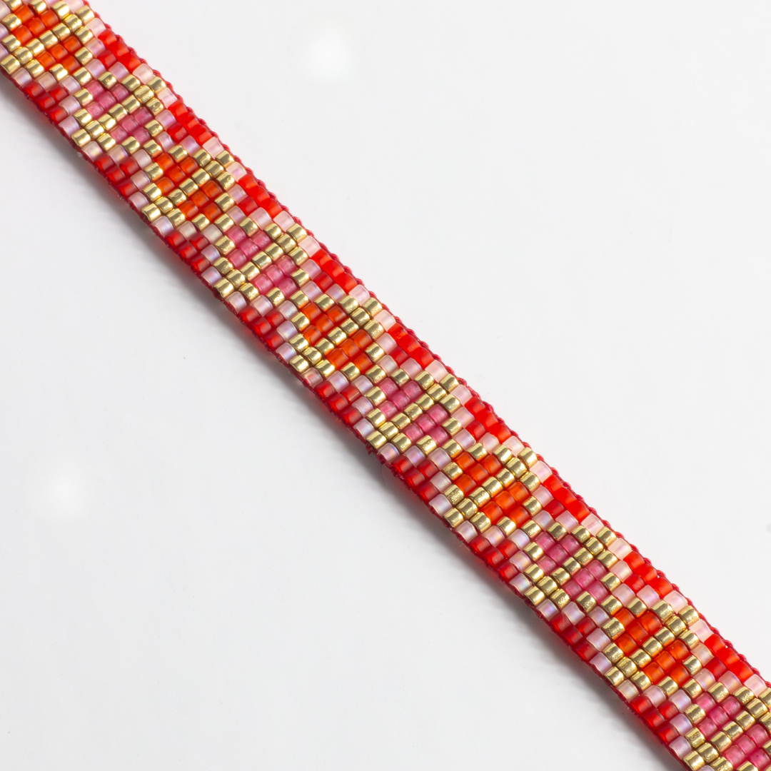 Close-up of hand-beaded Tatreez woven bracelet in orange-red, orange, bubblegum pink, pink mist and gold. Beadwork detail showing texture and pattern.