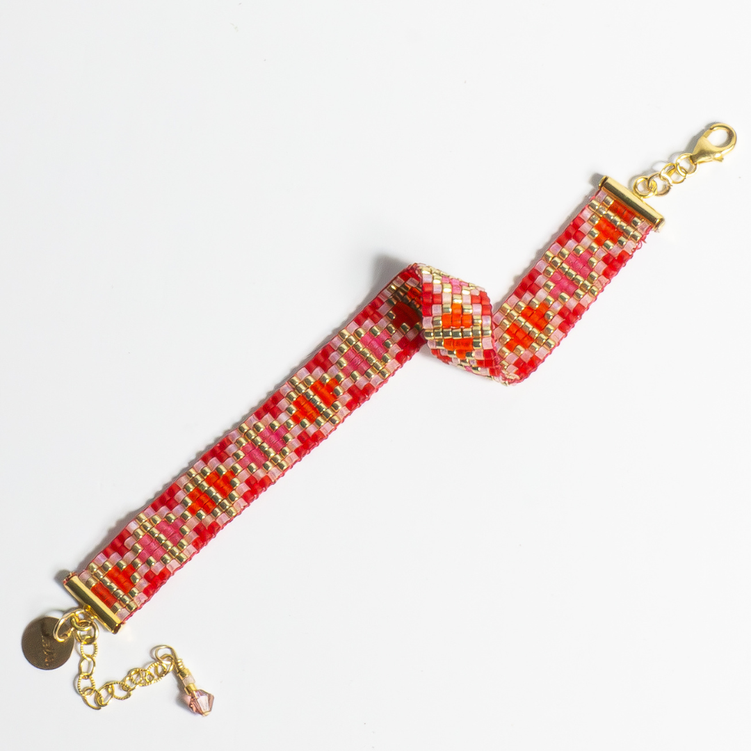 Hand-beaded Tatreez woven bracelet in orange-red, orange, bubblegum pink, pink mist and gold on white background. Full view. Available with adjustable stainless steel clasp or gold-filled lobster clasp.