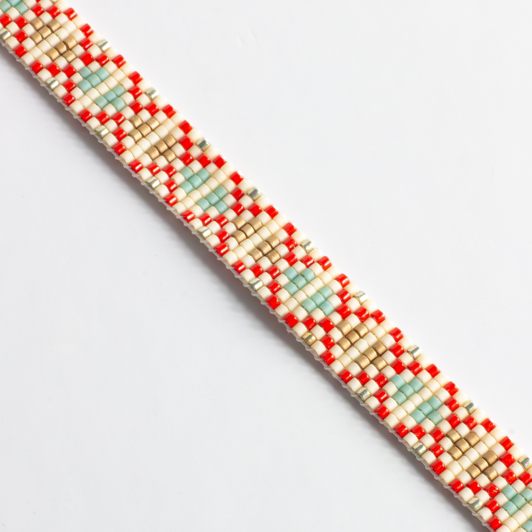 Close-up of hand-beaded Tatreez woven bracelet in true red, silver, antique beige, sea foam and champagne. Beadwork detail showing texture and pattern.